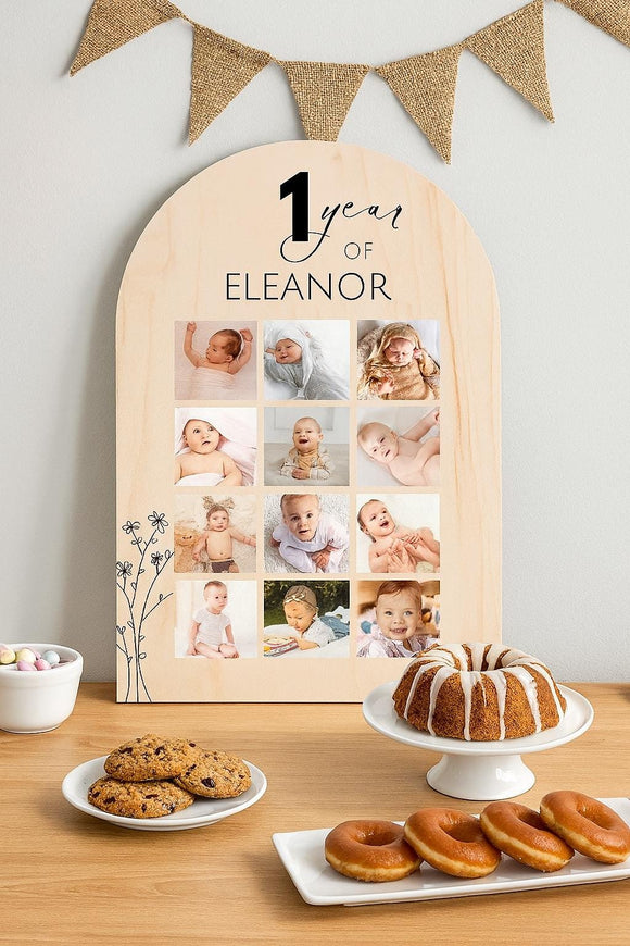 First birthday sign with 12-month baby photo collage leaning against wall on dessert table with bundt cake, cookies, and doughnuts